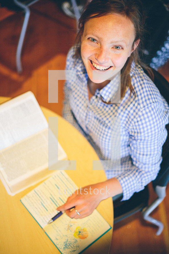 Woman sitting at a table, looking up smiling, studying her bible, making notes