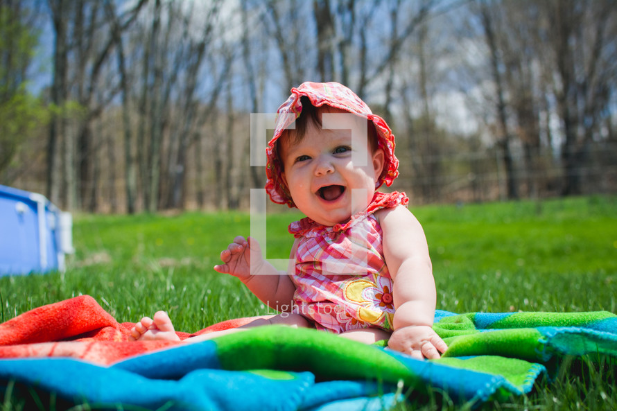 an infant girl sitting on a blanket in the grass