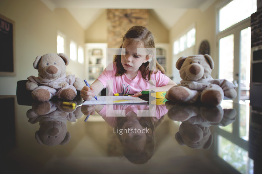 a little girl coloring with crayons and teddy bears 