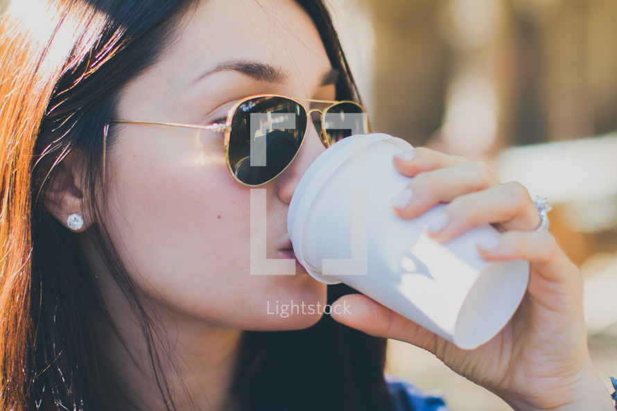 a woman in sunglasses drinking a cup of coffee 
