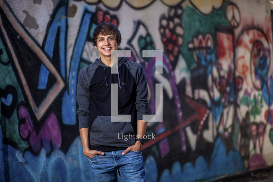 young man standing in front of a graffiti covered wall 