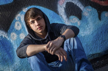 young man squatting in front of a graffiti covered wall 