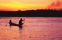 a man fishing with a net from his boat at sunset