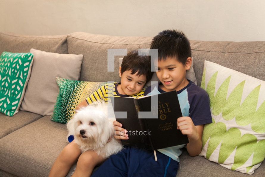 brothers sitting on a couch reading a Bible with their pet dog 