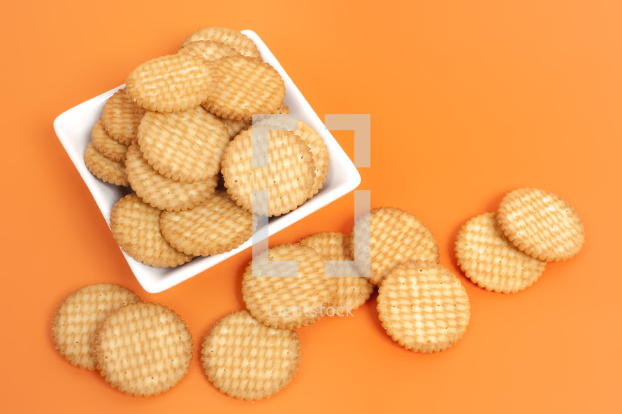 A white plate full of round crackers on an orange surface.