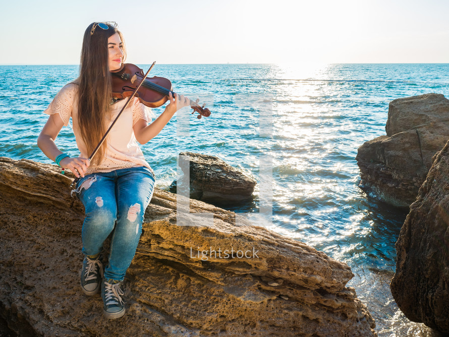 Young woman playing a violin on the beach.