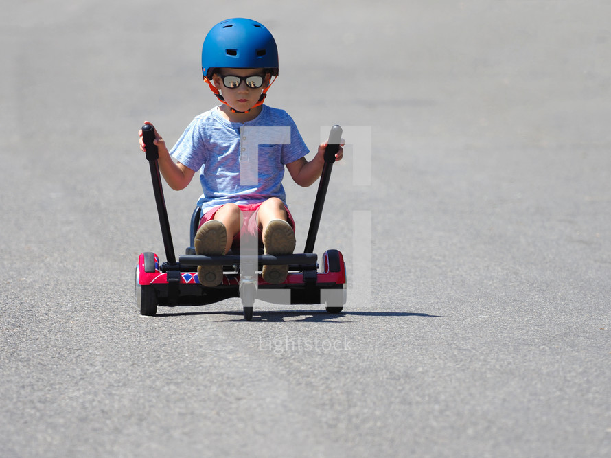 Happy boy standing on hoverboard or gyroscooter with kart accessory kit outdoor. New modern technologies