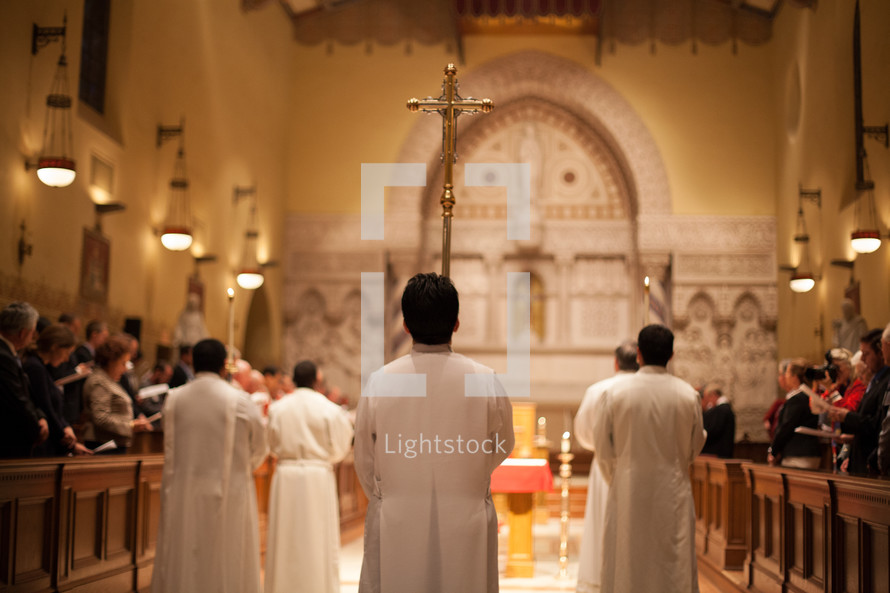 Catholic altar servers and priests exiting mass with a processional cross 