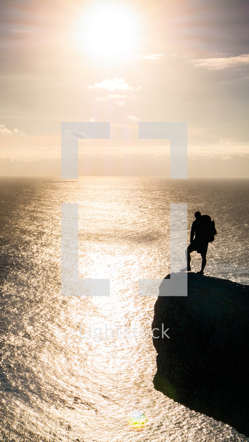silhouette of a man with a backpack on the edge of a sea cliff at sunset 