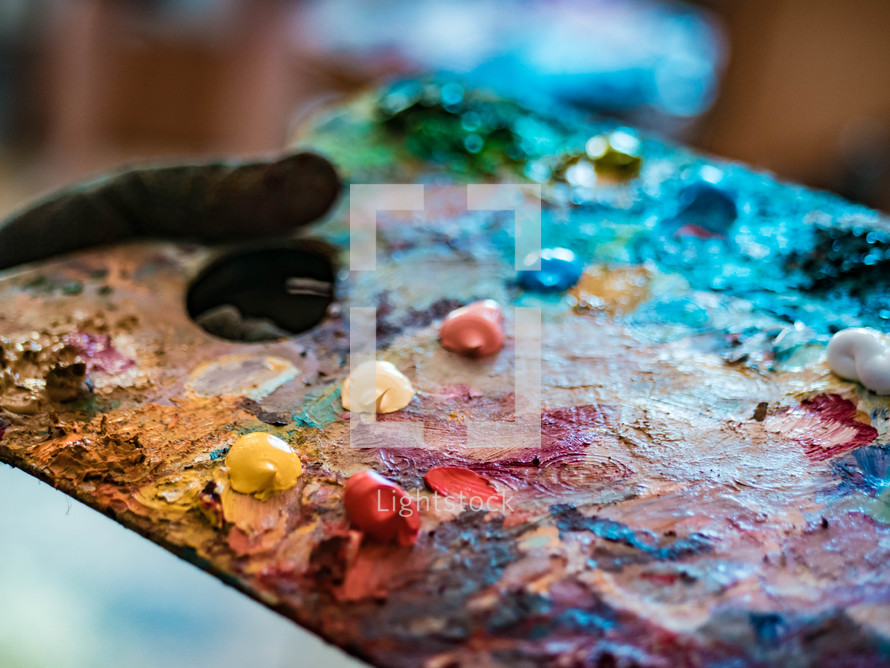 Wooden art palette with oil paints. Mixing colors together. Artistic instrument with many colors. Working tool with squeezed out tubes of paint.
