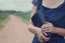woman standing on a dirt road holding a Bible 