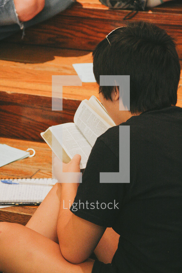 Teen reading the Bible while sitting on the floor.