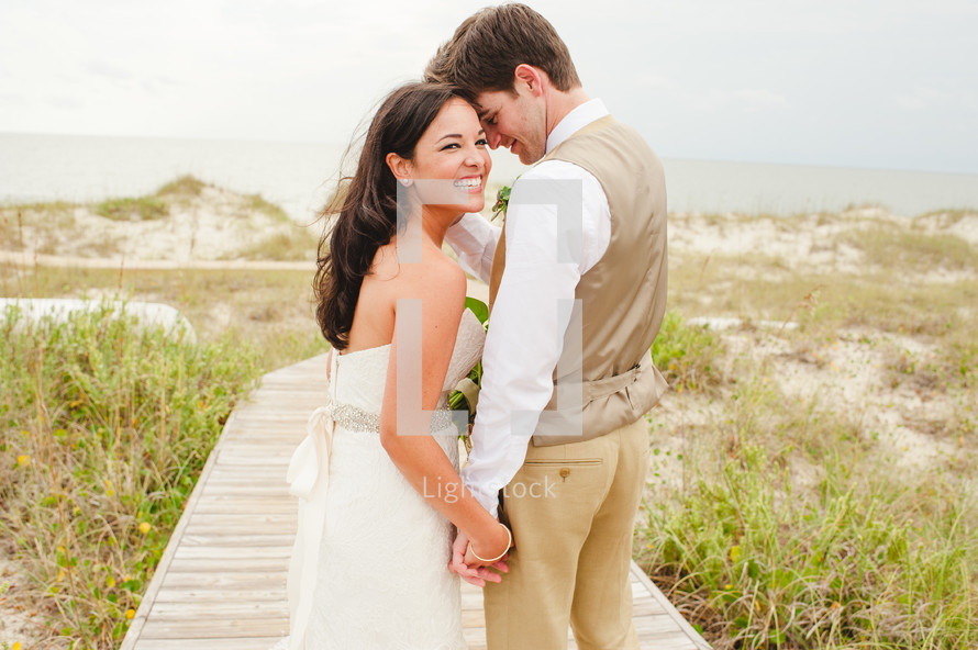 a bride and groom holding hands on a beach boardwalk 
