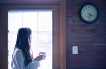 a woman standing in front of a window holding a mug of coffee 