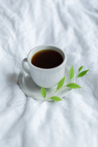 coffee cup, saucer, and sprig of a plant 