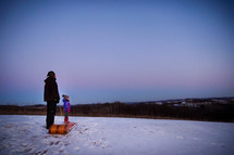 father and daughter sledding at sunset 