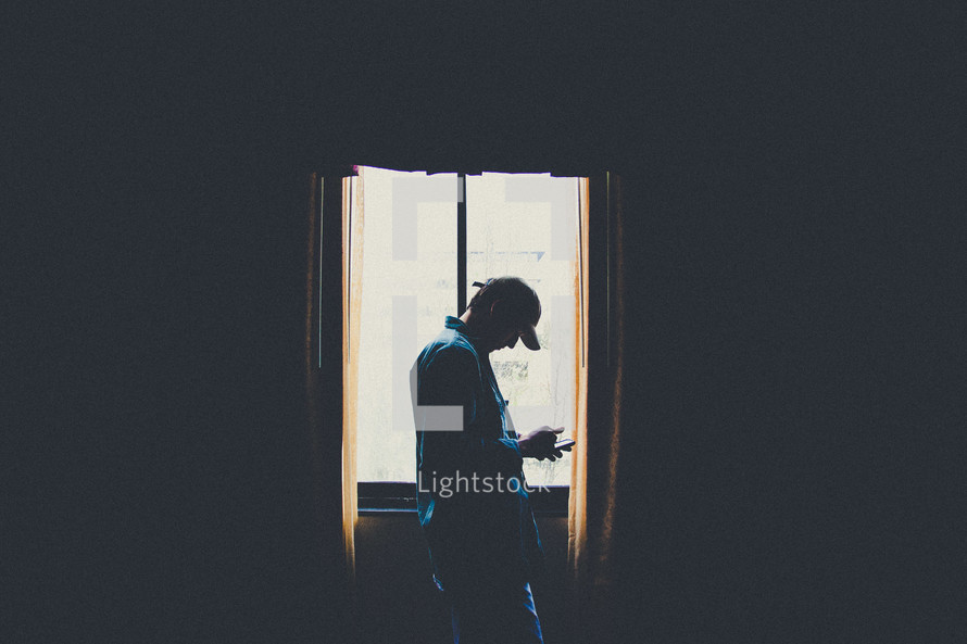 man checking his phone standing in a window 