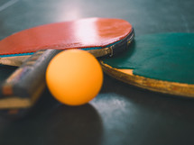 two ping-pong bats and a ball on a table tennis table.