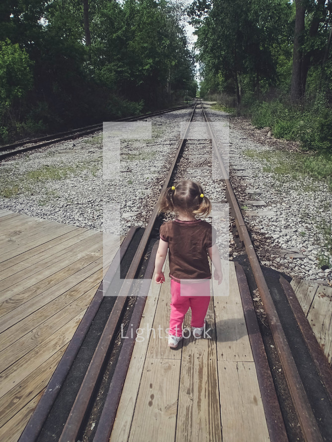 toddler girl standing in the middle of train tracks 