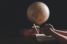 Wooden cross and hands on Bible with globe