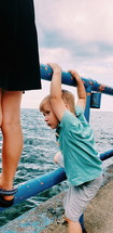 child looking over a railing at the ocean 