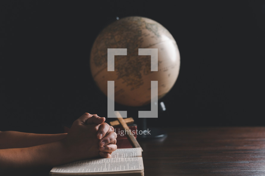 Wooden cross and hands on Bible with globe 