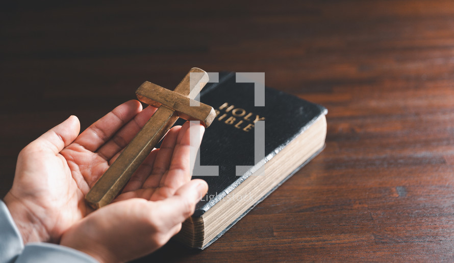 Wooden cross and hands on Bible