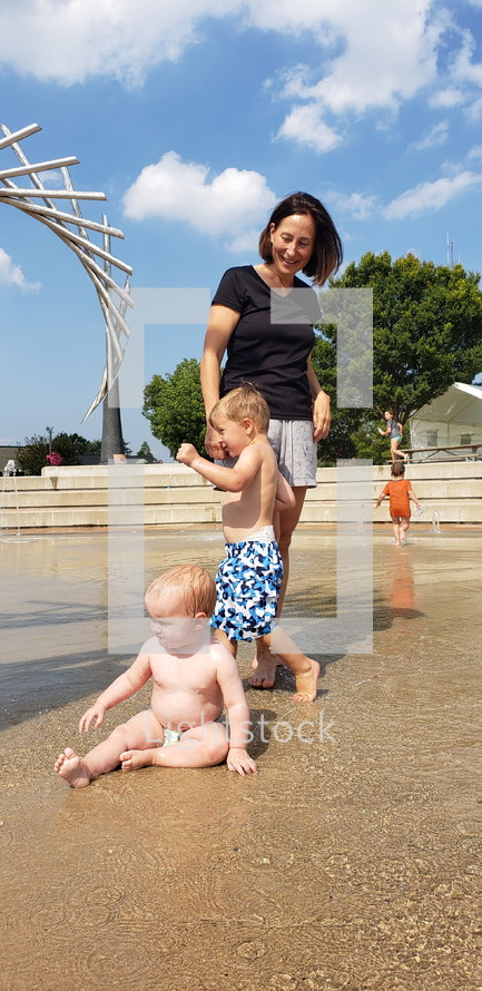 mother and toddlers playing at a splash park 