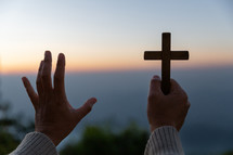 Person's raised hands holding a cross and praying