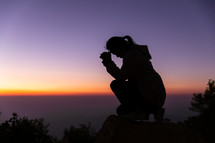 Woman kneeling in prayer at sunset
