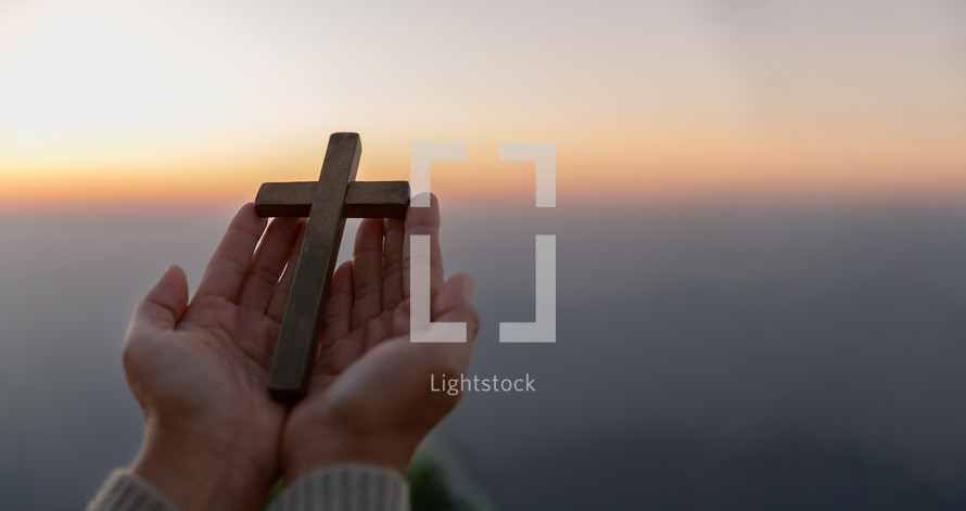 Person's hands holding a cross at sunset