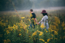 a couple holding hands walking through a field of flowers 