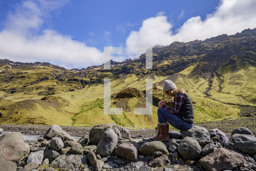 a woman sitting on a rock praying outdoors in Iceland 