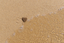 heart-shaped rock on sand lapped by water