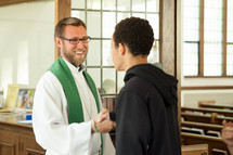 a priest greeting a teen boy 