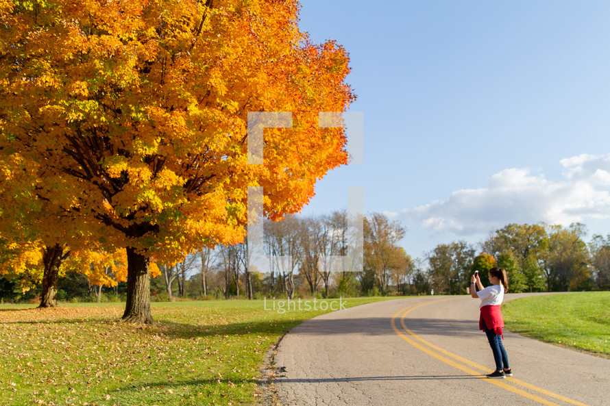 woman taking a picture of fall foliage 