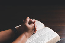 Hands clasped in prayer on Bible