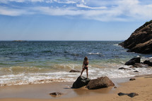 child standing on a rock at the beach 