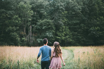 couple holding hands walking through a field 