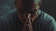 A man praying in a grey shirt with his eyes closed