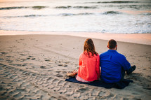 a couple sitting on a blanket in the sand at the beach 