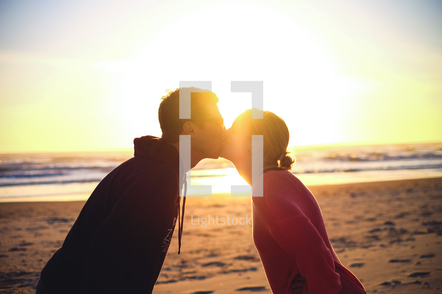 Sun shining on a couple kissing on a sandy beach.