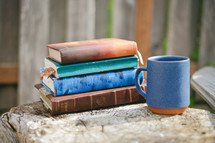 Stack of books and coffee cup on a tree stump.