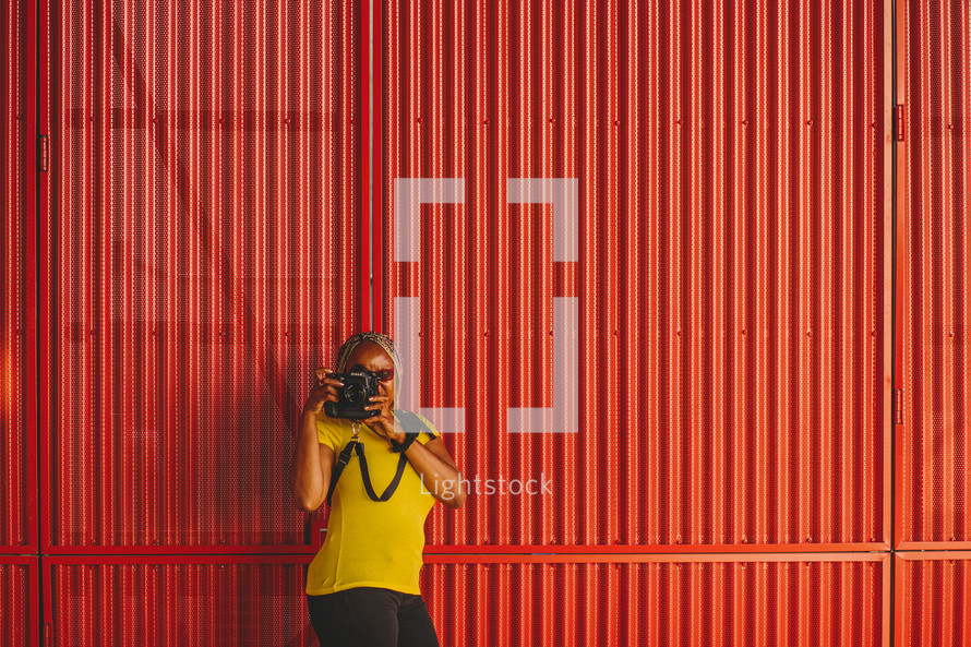 African-American woman taking a picture with a camera standing in front of a red wall 