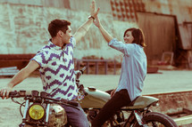 a man and woman on motorcycles giving each other a high five 