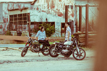 a man and woman in conversation next to their motorcycles 