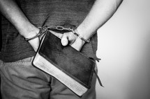 Handcuffed man holding a bible.