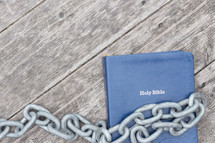 Bible and chain links on a wood background 