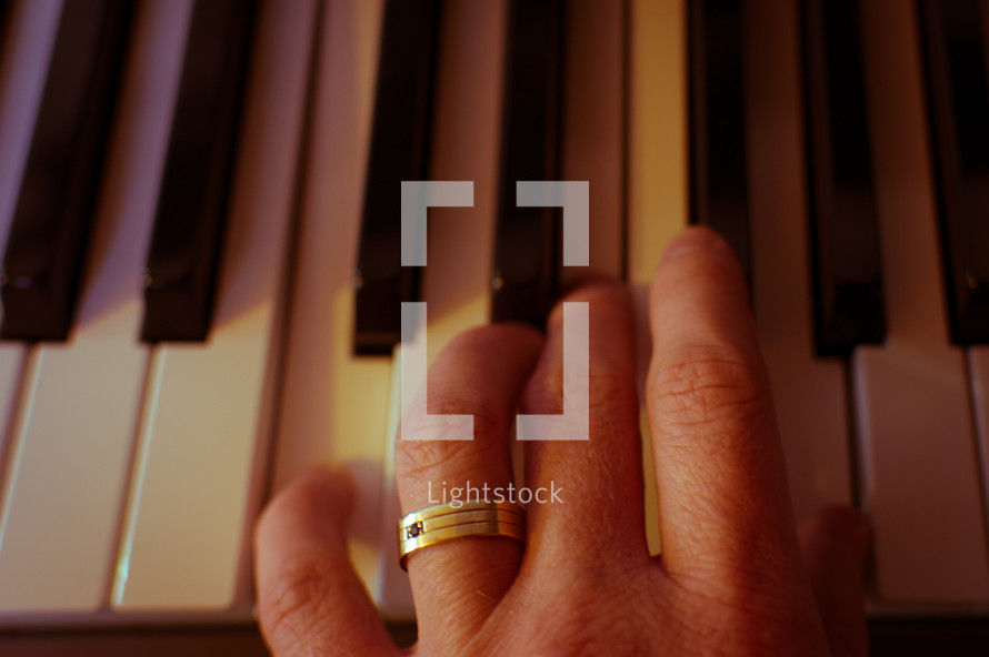 A hand (with wedding ring) plays a chord on a piano