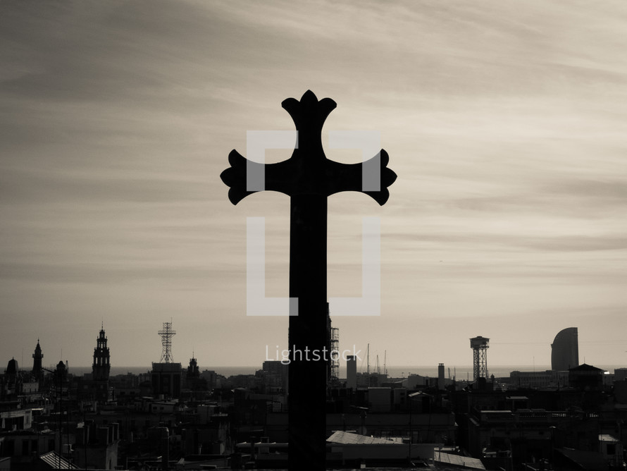 A gothic stone cross overlooking the sea-front city outlook, in black and white (b&w)